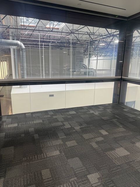 Conference-room glass wall at Upper Deck's Carlsbad office powered clear, with the open workspace visible through the switchable film