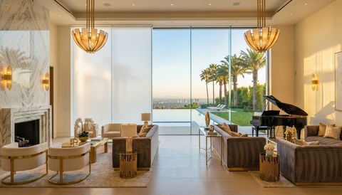 Beverly Hills estate with a floor-to-ceiling clear switchable smart glass wall overlooking palm-lined grounds and an infinity pool — several glass panels switched to frosted privacy mode