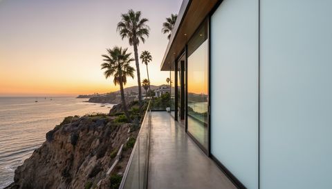 Luxury California coastal-bluff home with floor-to-ceiling clear switchable smart glass framing the Pacific Ocean and palms at golden hour — several glass panels switched to frosted privacy mode