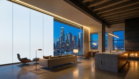 Downtown Los Angeles high-rise loft with a floor-to-ceiling clear switchable smart glass wall overlooking the skyline at blue hour — several glass panels switched to frosted privacy mode