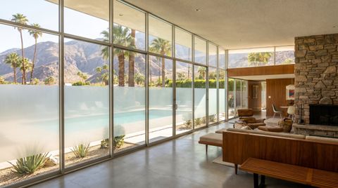 Riverside County desert resort home with a floor-to-ceiling clear switchable smart glass wall framing a palm-lined pool and the San Jacinto mountains