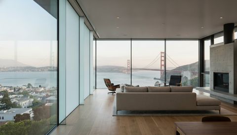 San Francisco home with a floor-to-ceiling clear switchable smart glass wall framing the Golden Gate Bridge and bay — several glass panels switched to frosted privacy mode