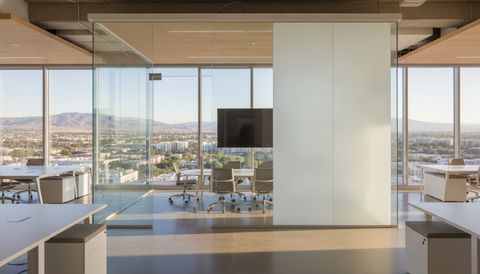 Downtown San Jose tech office with a switchable smart glass conference room wall — the left panels clear over the Santa Clara Valley foothills, the right panels switched to flat, evenly frosted milky-white privacy