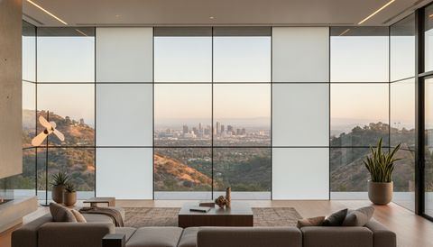 Modern Torrance single-family living room with a wall of switchable smart glass opening to the backyard — half the panels crystal clear, half switched to flat, even, milky-white frosted privacy mode