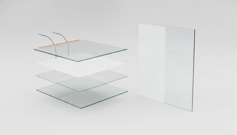 Illustration: an exploded view of a laminated smart glass panel — the outer glass sheet with its copper busbar and two low-voltage leads, the milky PDLC smart-film core, the interlayer, and the inner glass sheet — beside the assembled panel with one half frosted an even milky white and the other half fully clear