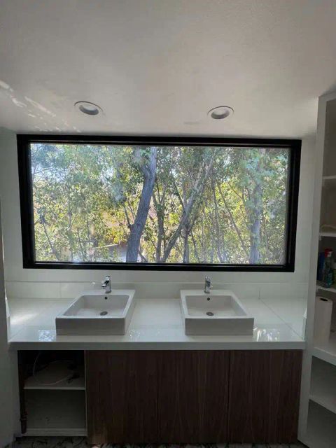 Smart glass bathroom window in Pasadena in clear mode showing outdoor trees above double vanity sinks
