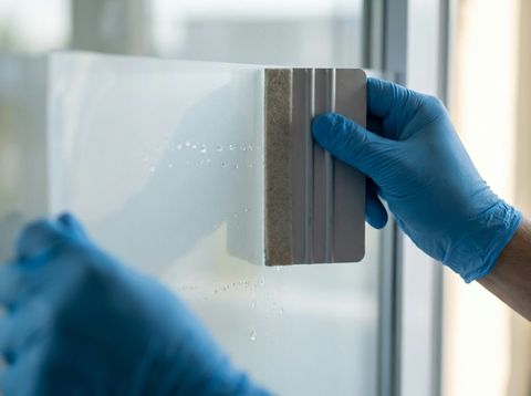Gloved hands squeegeeing switchable smart film flat onto glass to avoid trapped air