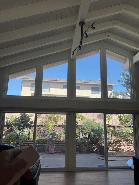 Hand holding the remote below clear Irvine gable windows, sky and neighboring house visible