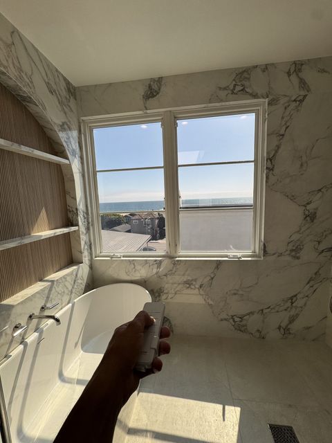 Hand holding a Smart View remote in a smart glass bathroom in Hermosa Beach, casement window clear with the ocean beyond
