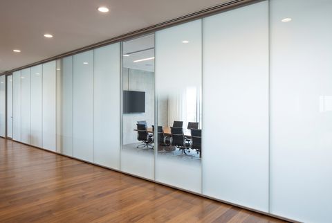 Illustration: a glass conference-room partition drawn in two states, with one section of the wall clear and the adjoining section switched to an even frosted privacy finish