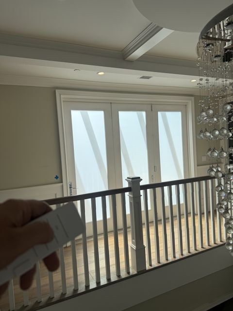 The handheld remote held up on the Studio City landing with the smart glass bifold door frosted, daylight still crossing the wood floor