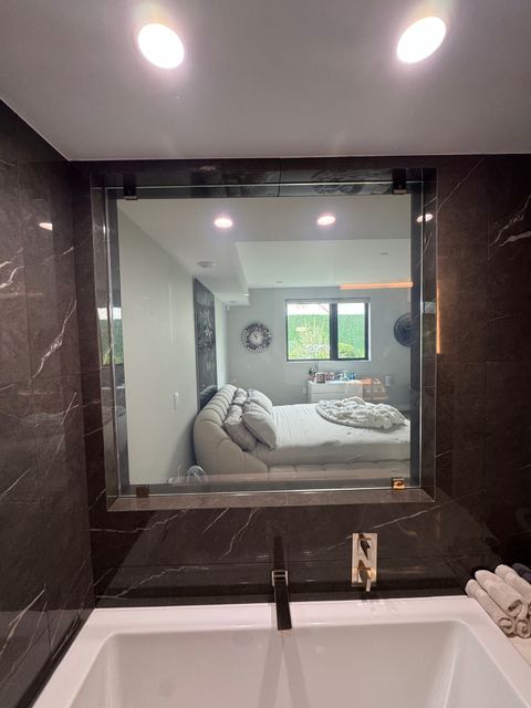 Smart glass bathroom in West Hollywood, the square panel above the marble tub clear and open to the bedroom beyond