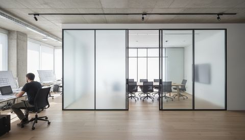Illustration of an interior glass partition wall in a daylit architecture studio, two tall panels frosted an even milky white and two panels clear showing the meeting room beyond
