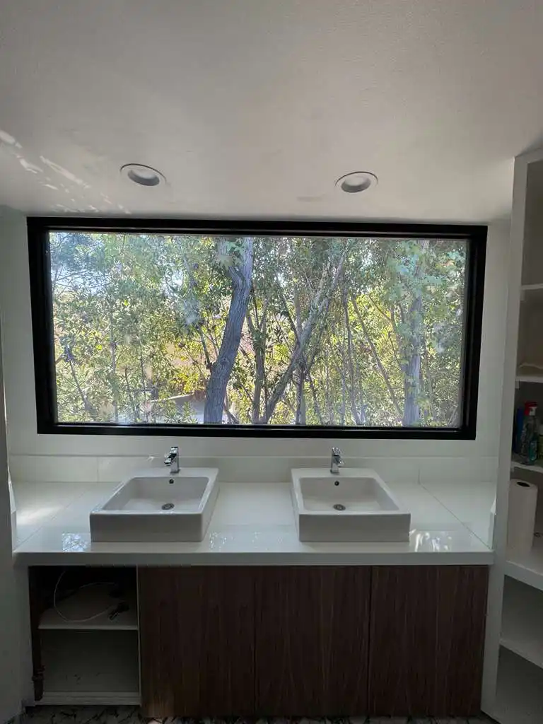 Smart glass bathroom window in Pasadena home in clear mode with outdoor tree view above double sinks
